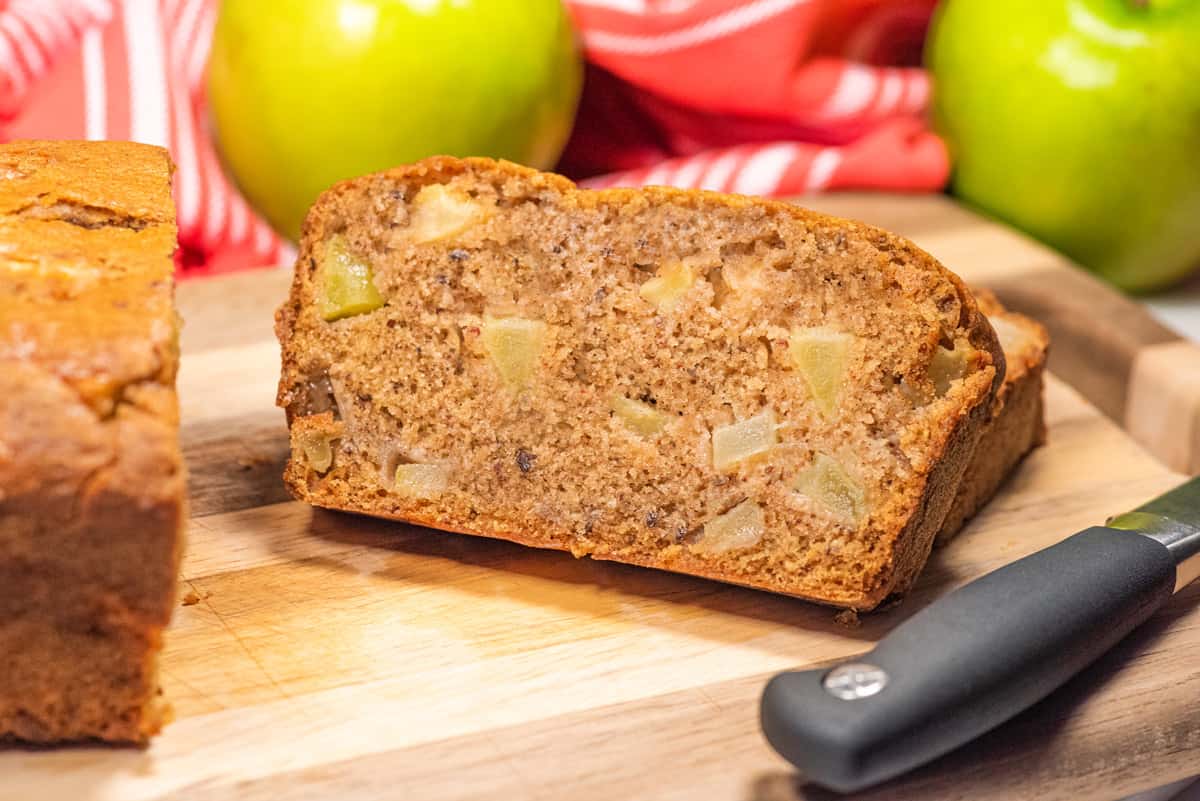 Slices of apple cinnamon bread on a cutting board with a green apple in the background.