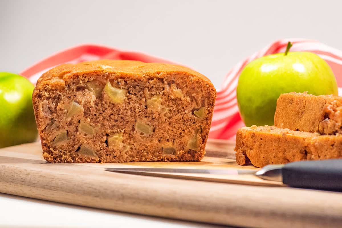 A loaf of apple cinnamon bread with slices of the bread next to it and a knife laying in front.