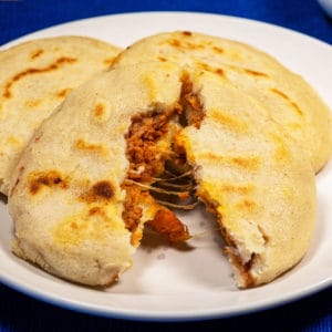 Plate of vegan pupusas with the cheesy center of a pupusa showing in the as the main pupusa.