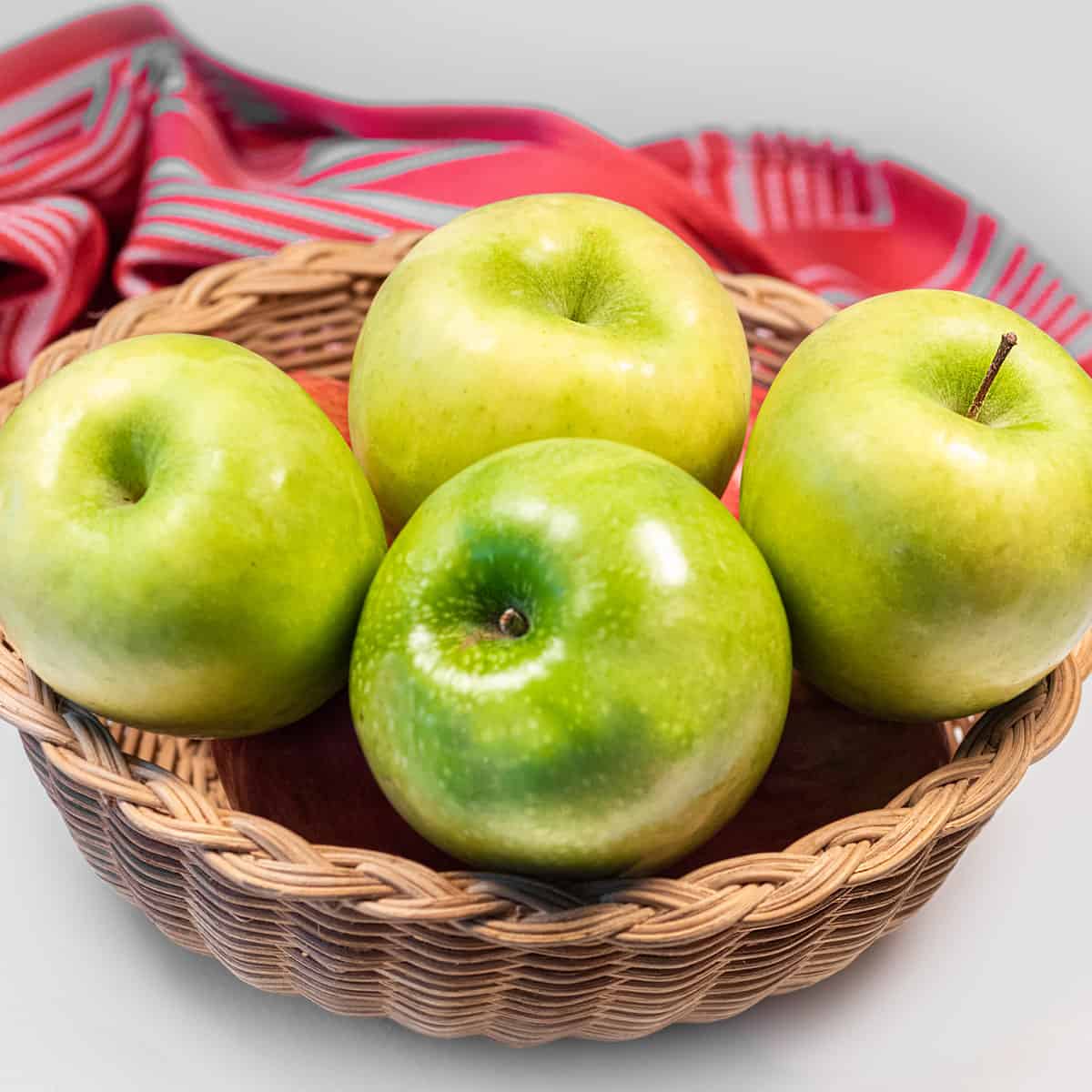 Basket of green apples with a red cloth in the background.