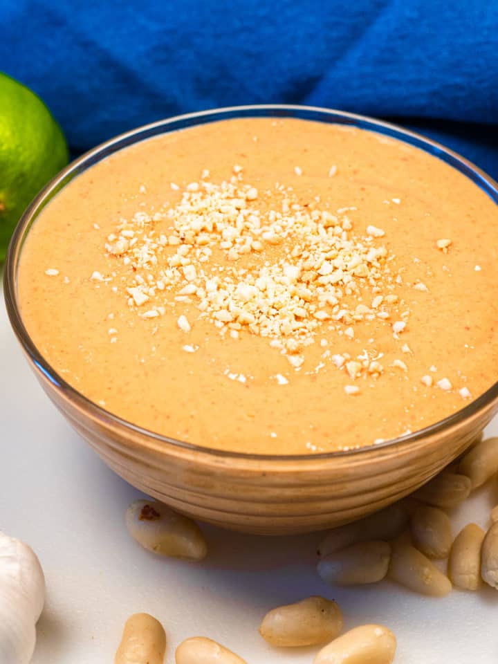 Peanut sauce in a dish with peanut laid around it, a lime, and clove of garlic.