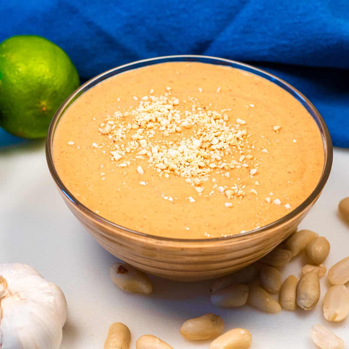 Peanut sauce in a dish with peanut laid around it, a lime, and clove of garlic.