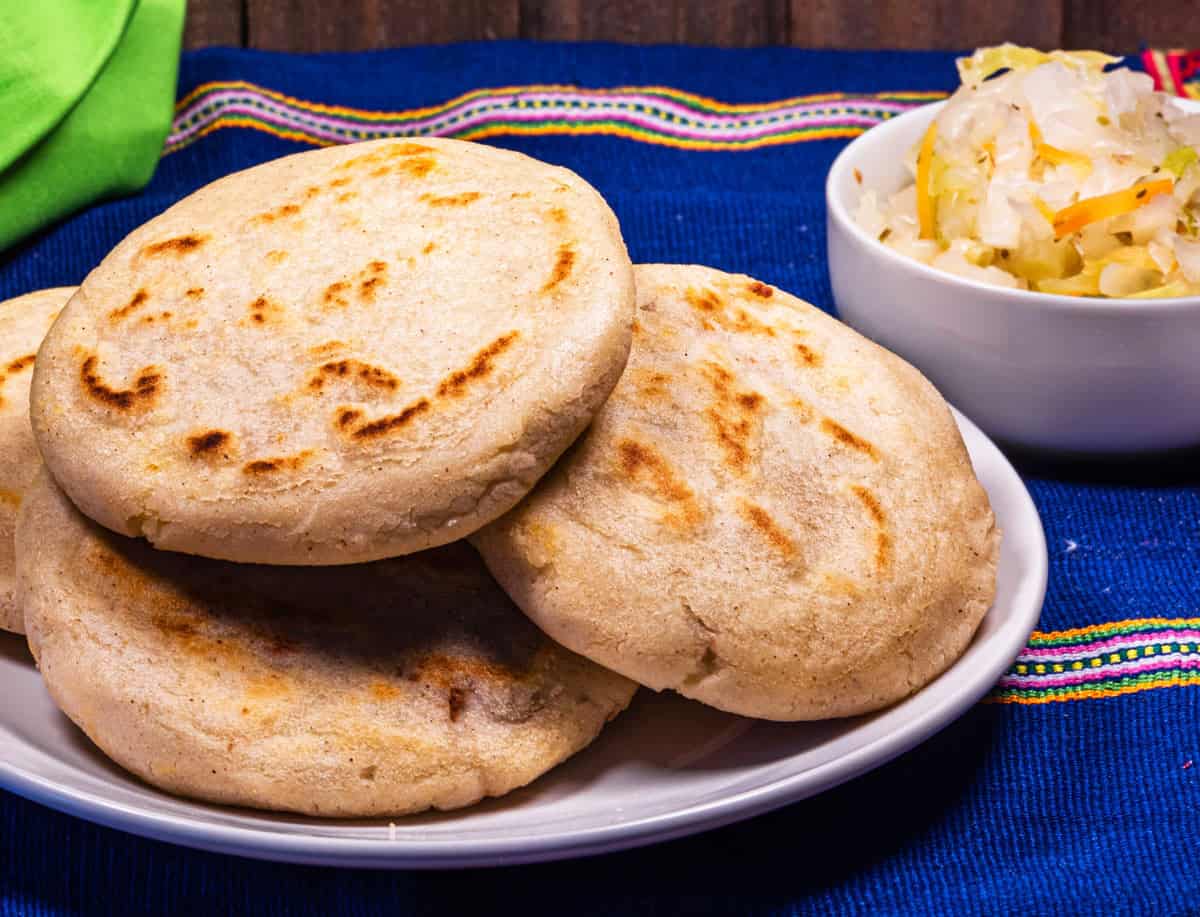 3 pupusas on a plate with a dish of cutido on the background.