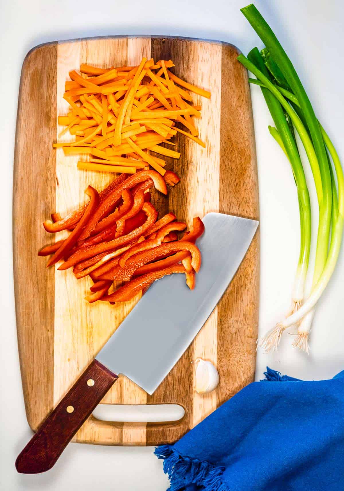 Julienned carrots and red bell pepper on a cutting board with a knife.