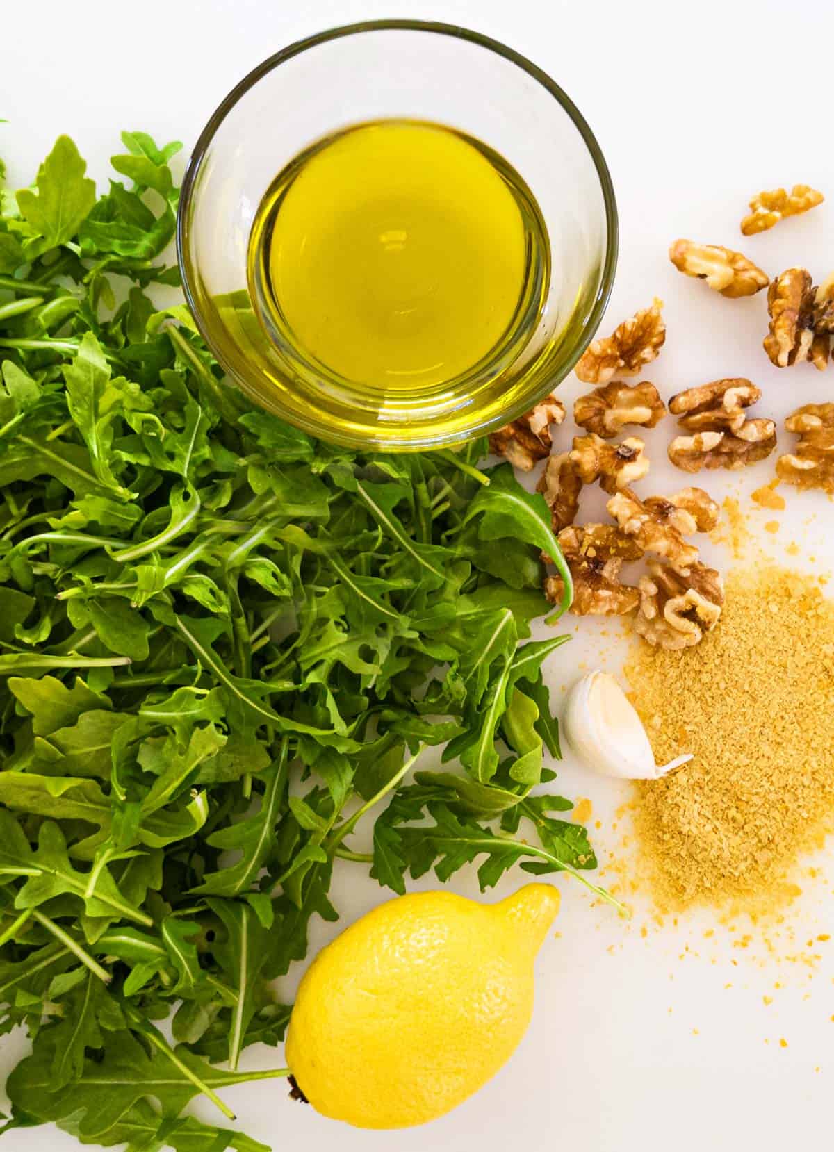 Arugula, olive oil, lemon, walnuts, and nutritional yeast laid out on a cutting board