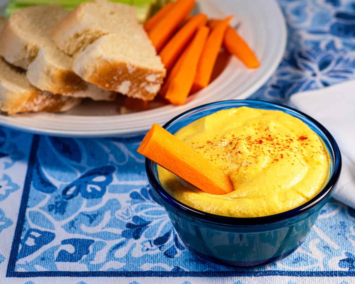 Vegan cashew cheddar cheese dip in a blue bowl with a carrot.
