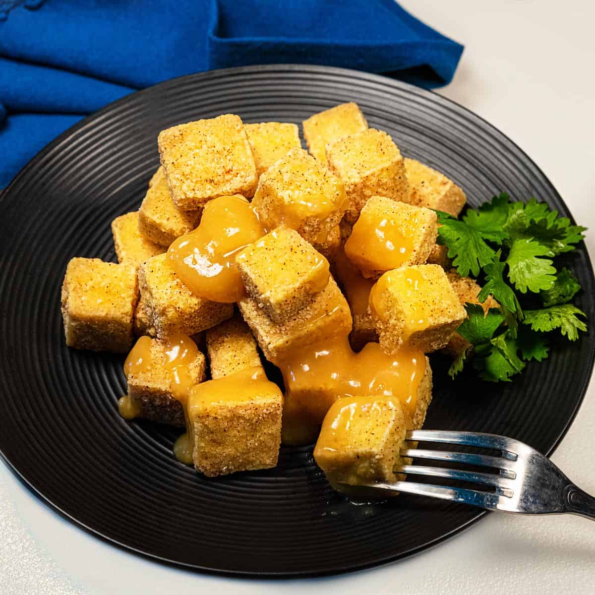 Plate of crispy tofu bites with orange sauce.