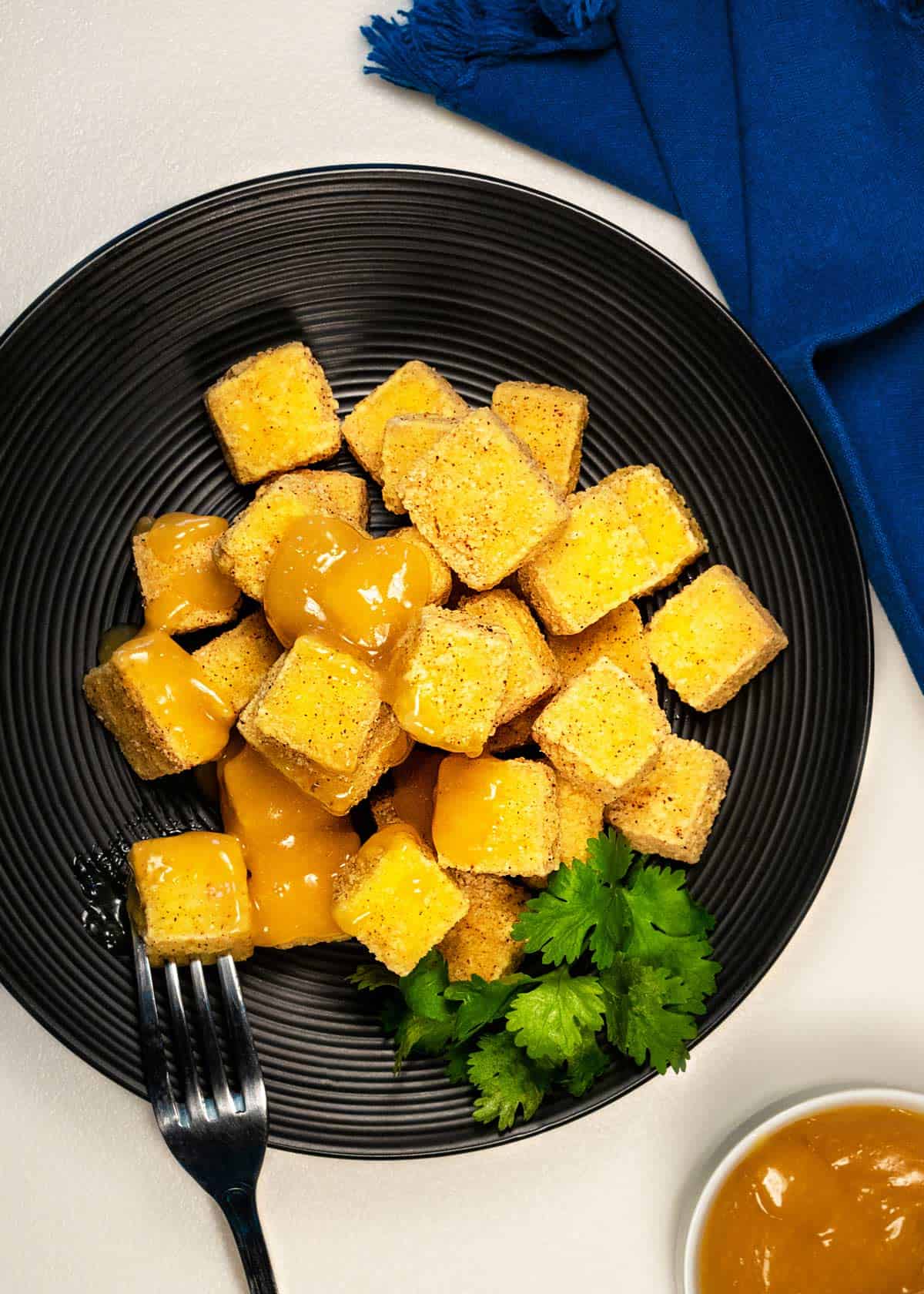Plate of crispy tofu bites with orange sauce.