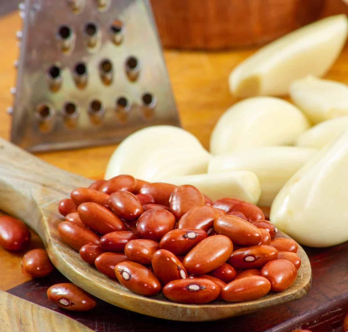 Wooden spoon with dry red beans and cloves of peeled garlic in the background.