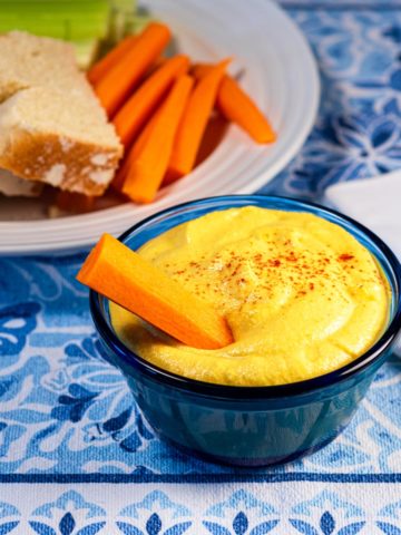 Vegan cashew cheddar cheese dip in a blue bowl with a carrot.