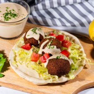 Falafel on a pita with shredded lettuce and diced tomatoes topped with tahini sauce.