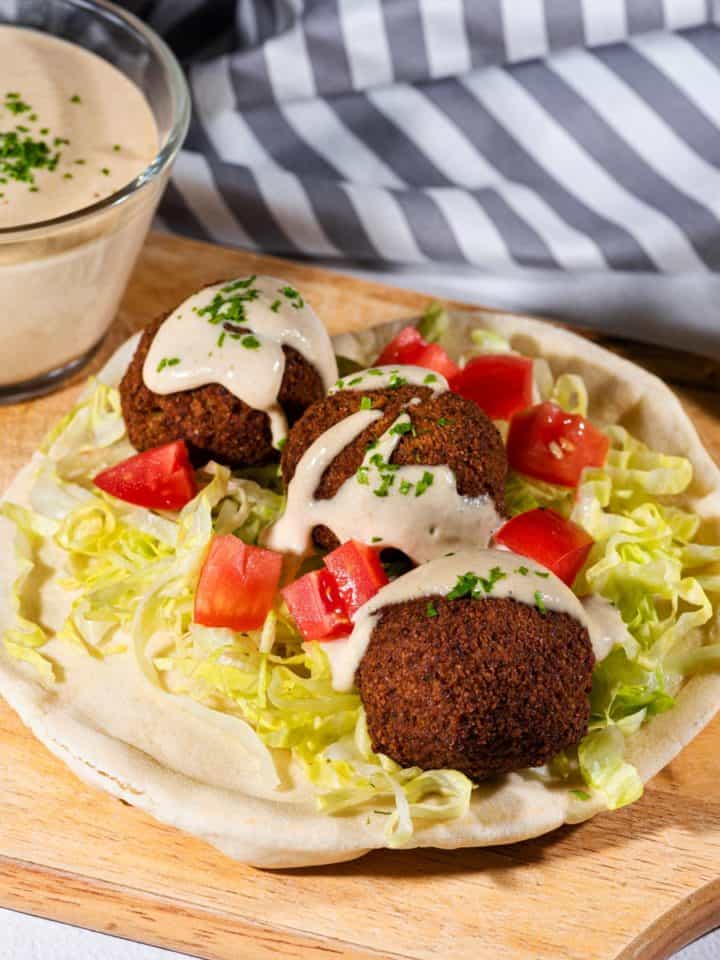 Falafel on a pita with shredded lettuce and diced tomatoes topped with tahini sauce.