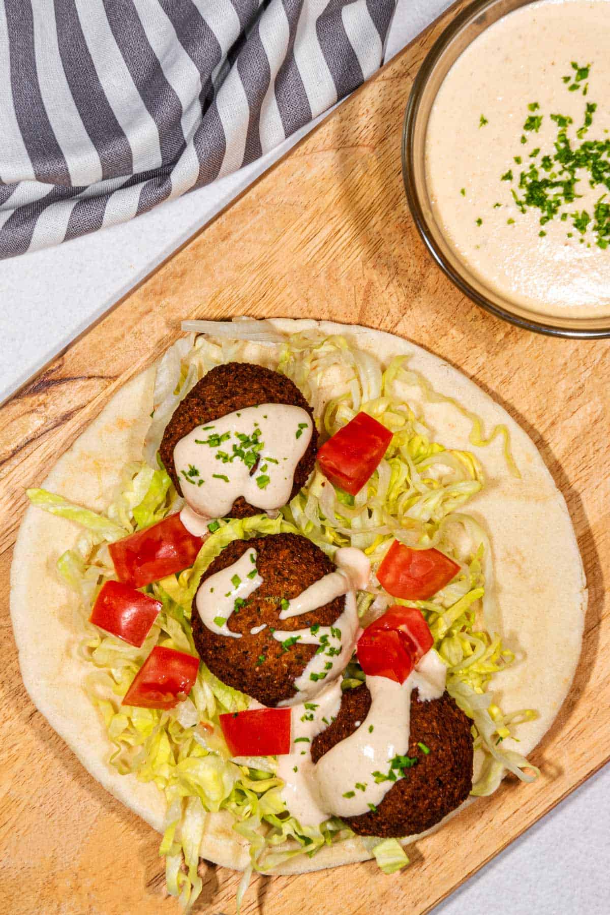 Vegan Falafel on a pita with shredded lettuce and diced tomatoes topped with tahini sauce.