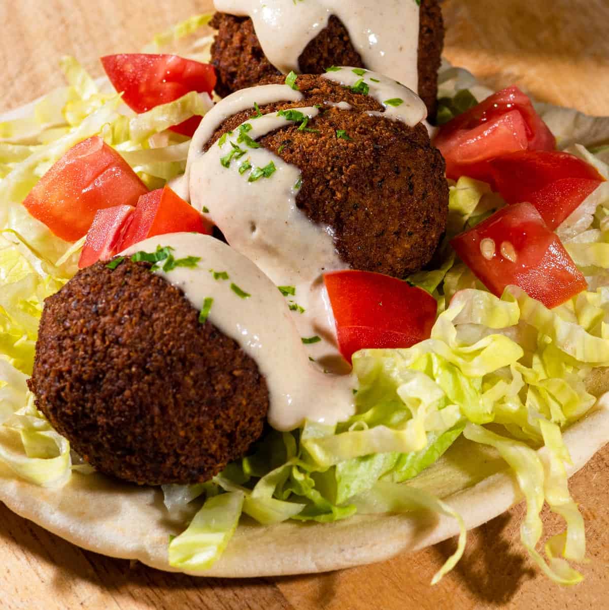Vegan Falafel on a pita with shredded lettuce and diced tomatoes topped with tahini sauce.