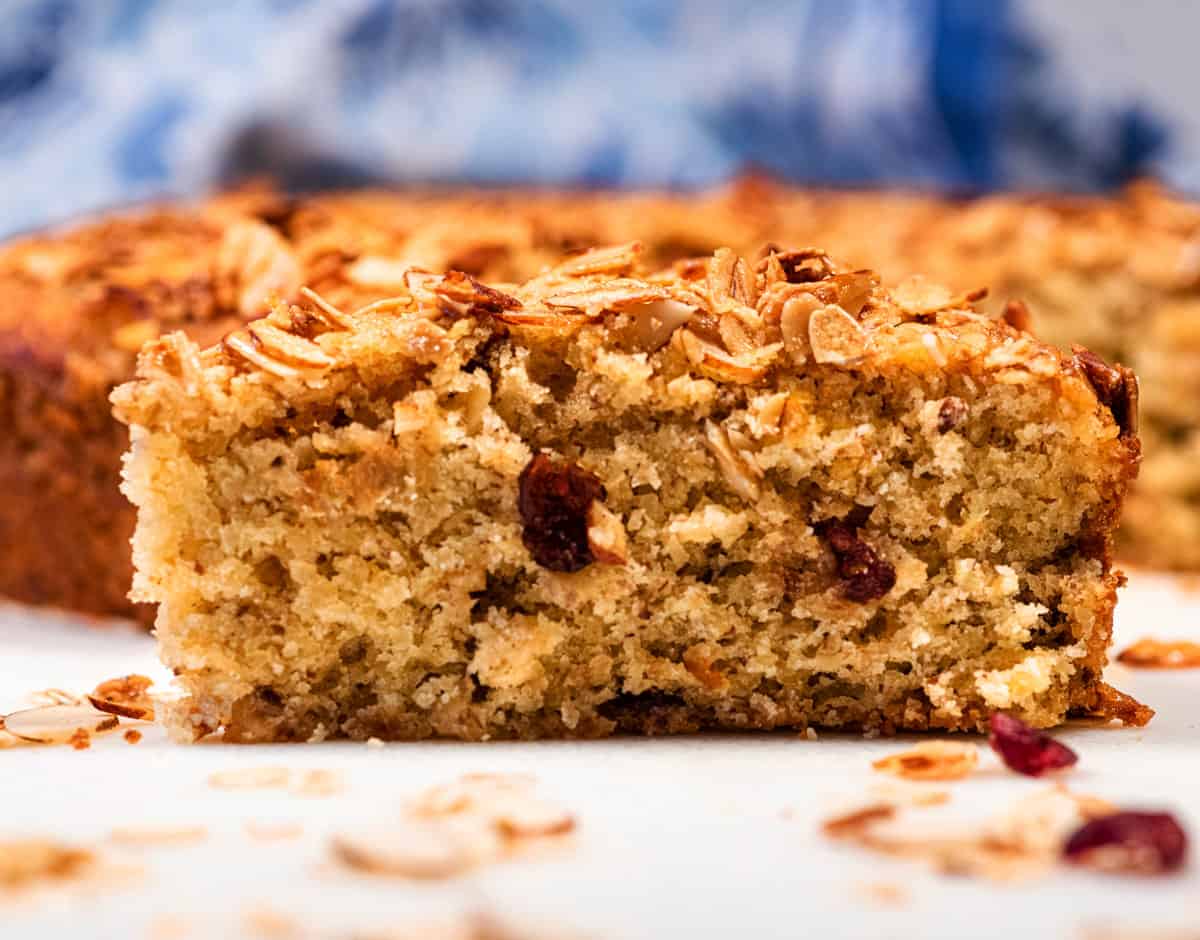 A vegan cranberry orange oatmeal cake with a slice cut out laying on the table.