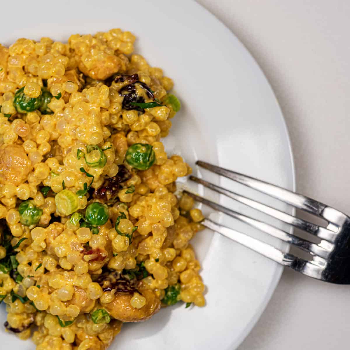 Dish of vegan curried Israeli couscous salad with cashews and cranberries.