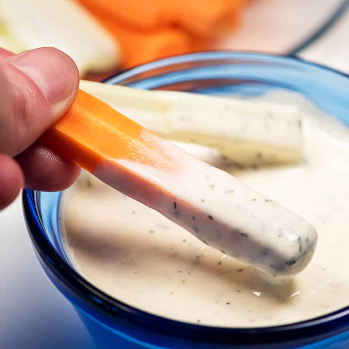 Dish of vegan ranch dressing with a carrot stick and celery stick dipped in it.