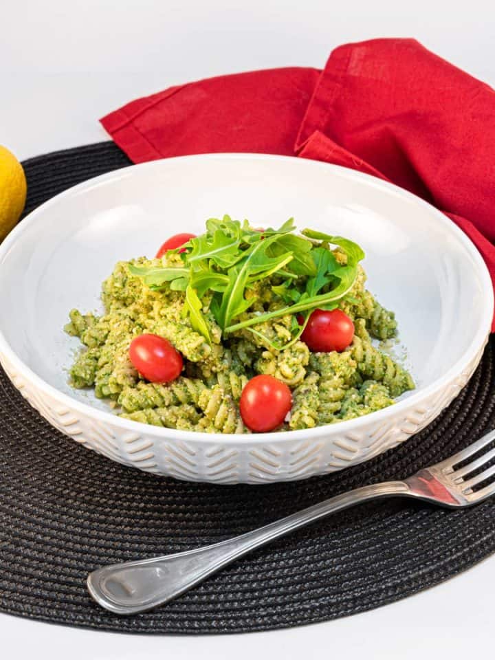 Bowl of vegan pesto pasta topped with arugula and tomatoes.