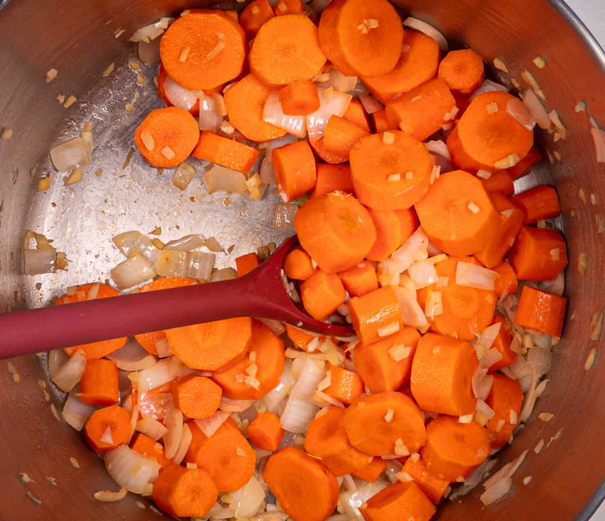 Onions and carrots sauteing in a pot.
