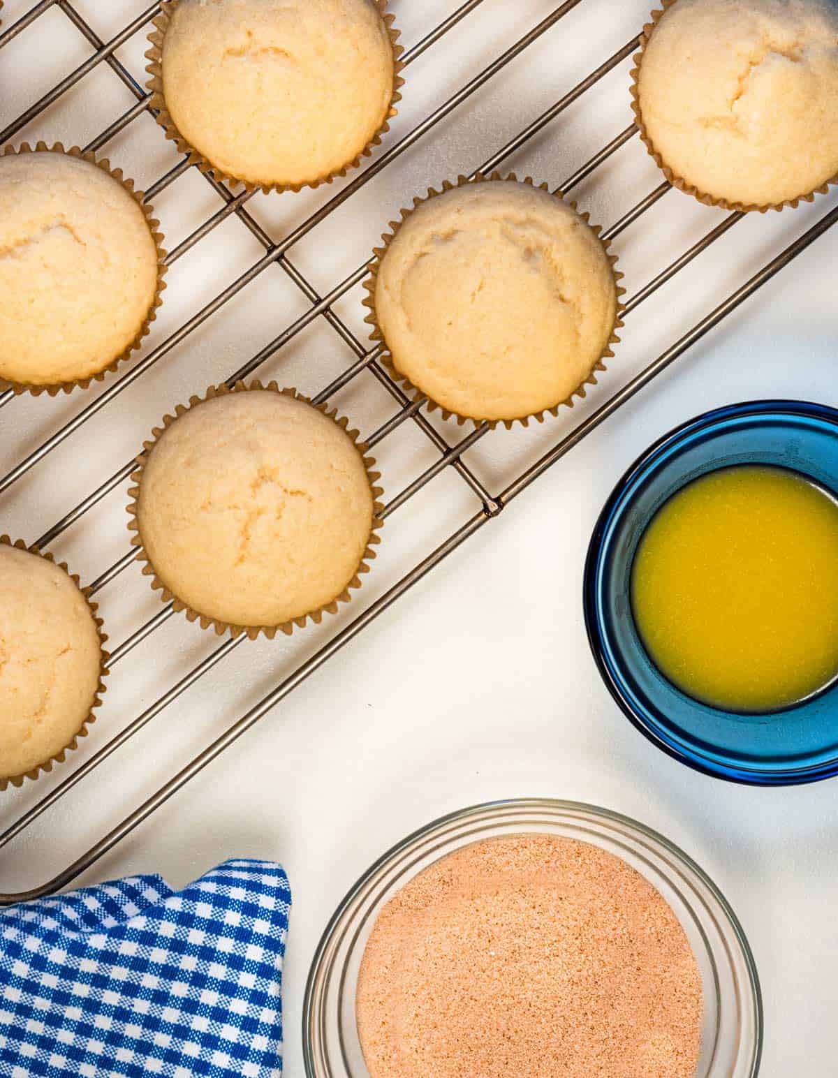 Muffins on a cooling rack with a dish of melted butter next to them and a dish of cinnamon and sugar.