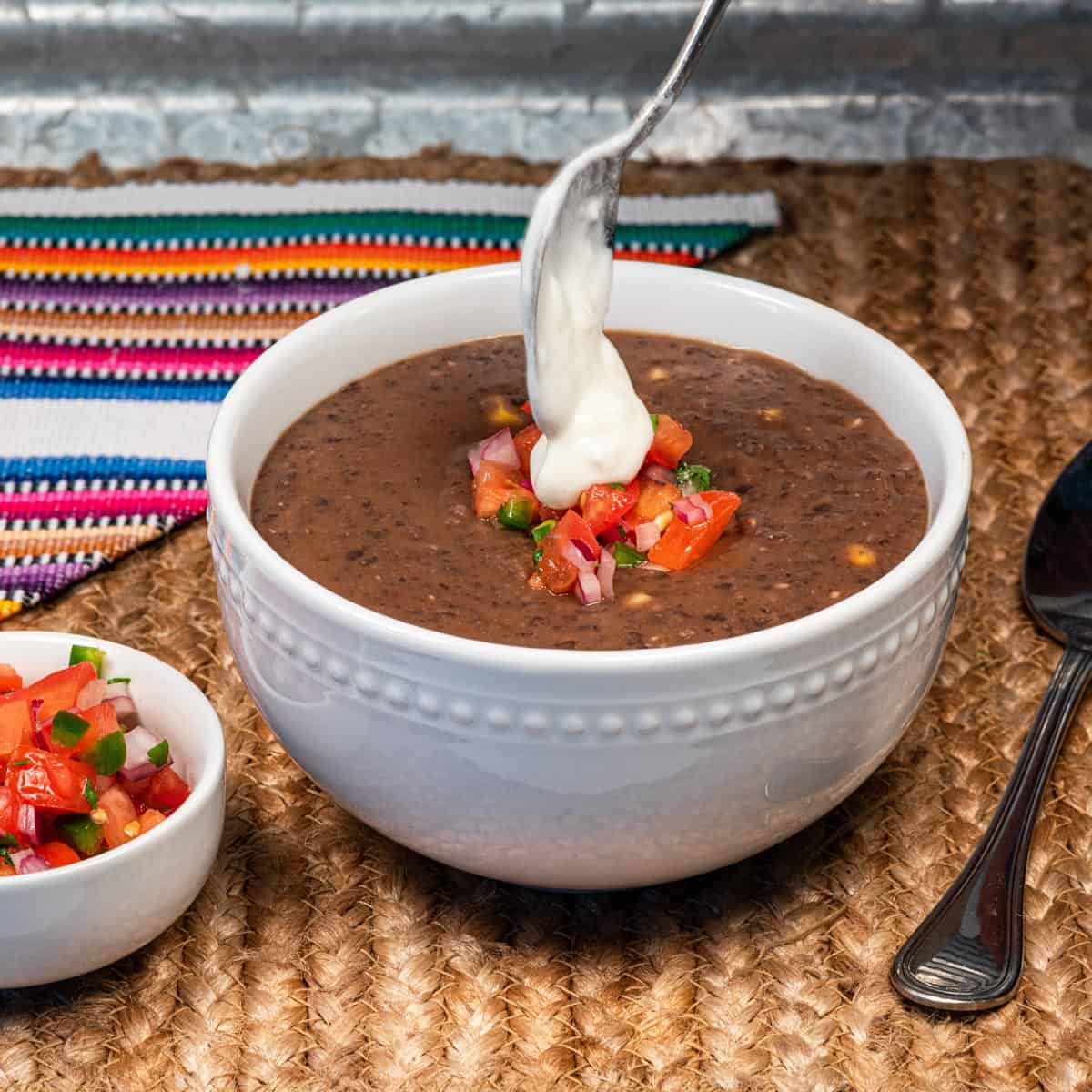 A bowl of vegan chipotle black bean soup being topped with vegan sour cream.