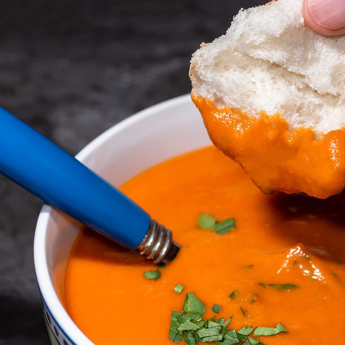 Bowl of vegan tomato soup with bread being dipped.