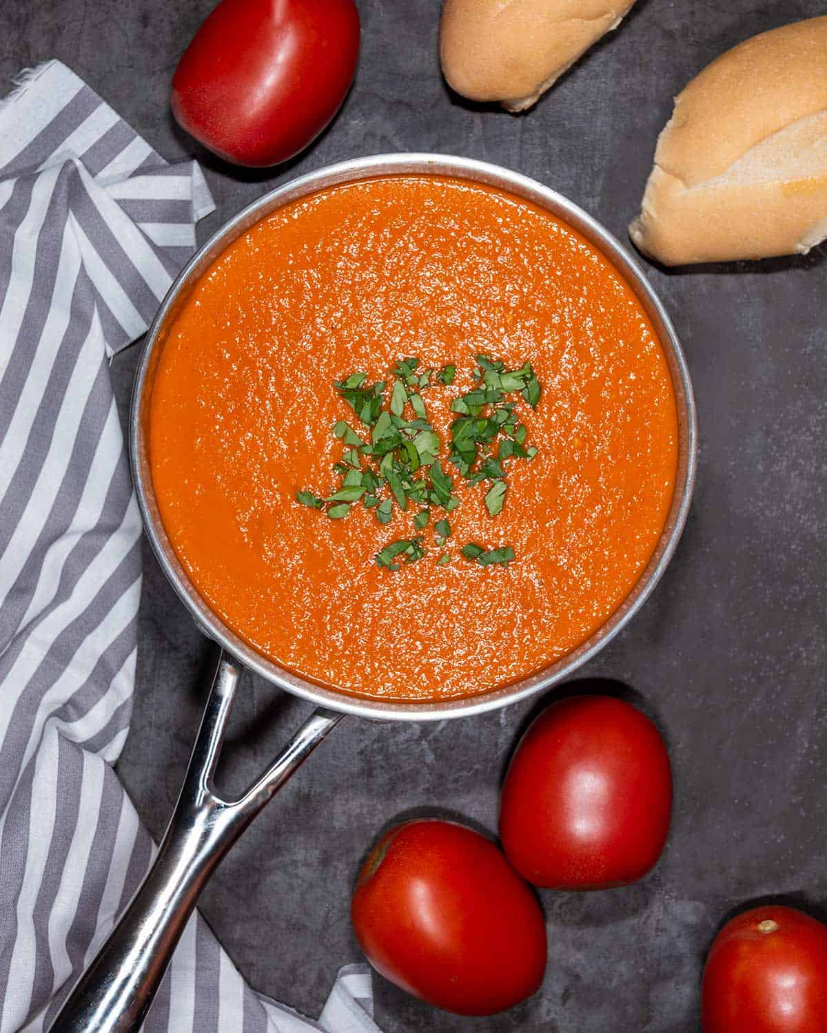 Pot of vegan tomato soup with bread and roma tomatoes in the background.
