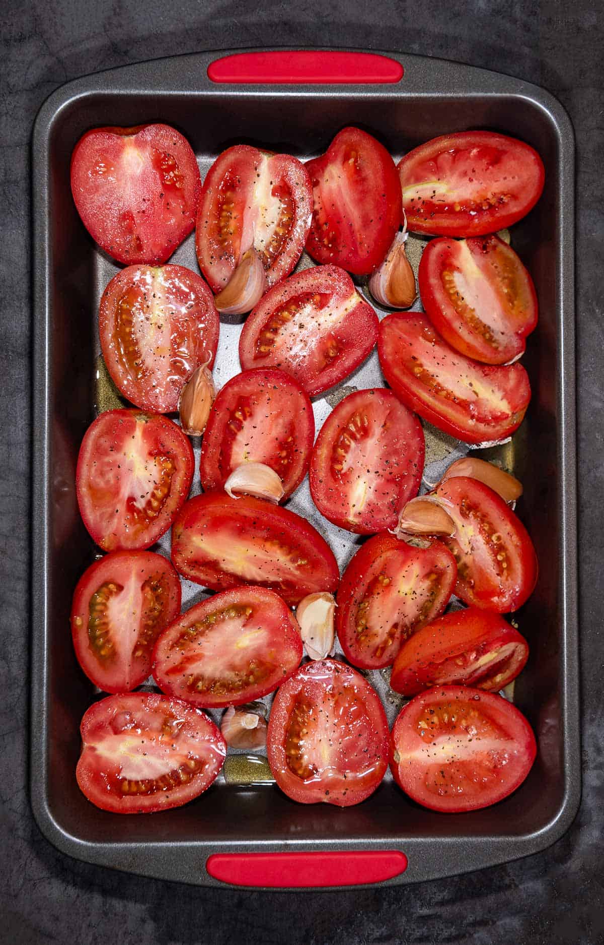 Roasting pan of roma tomatoes cut in half and garlic cloves ready to go in the oven to roast.