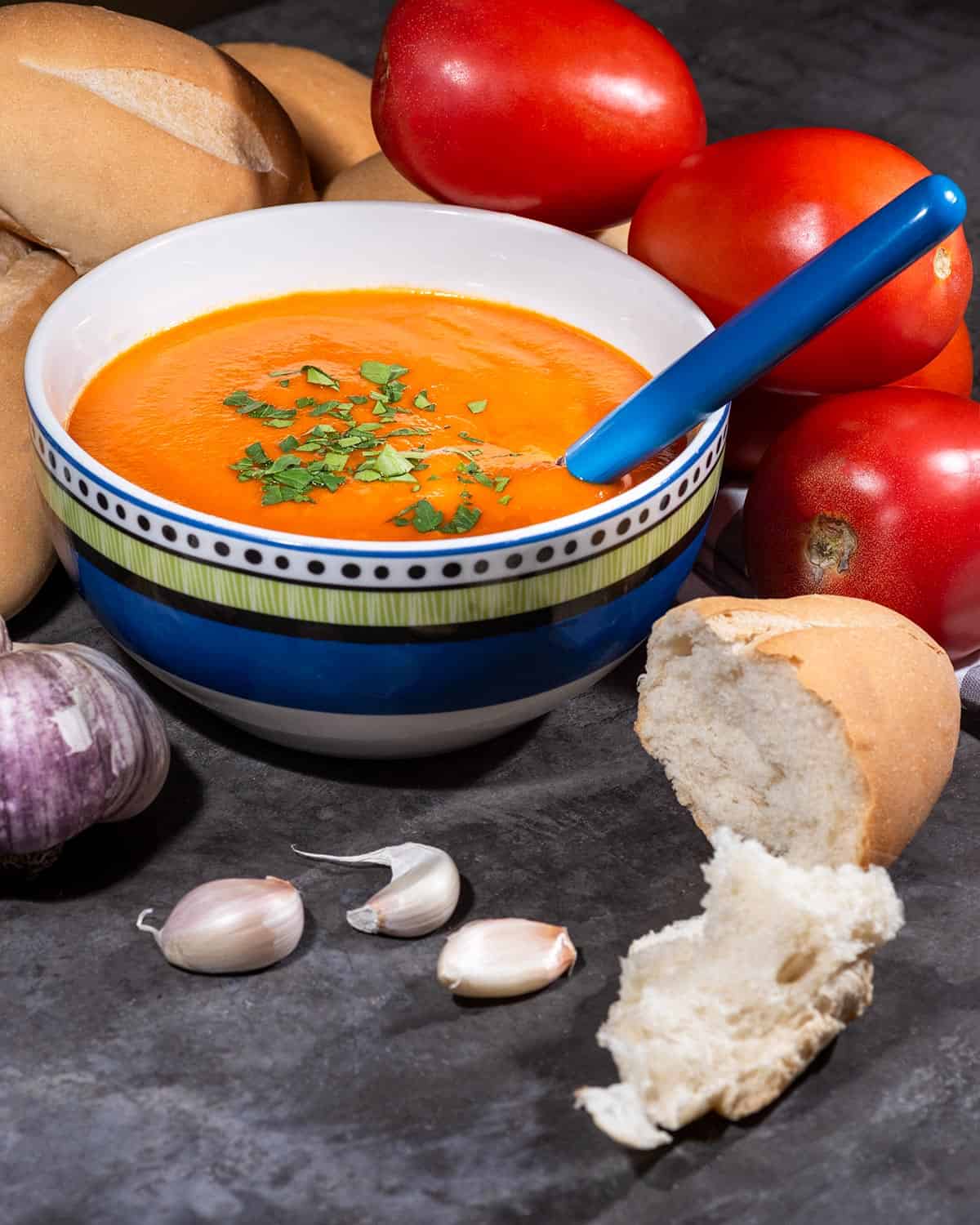 Bowl of vegan tomato soup with bread and roma tomatoes in the background.
