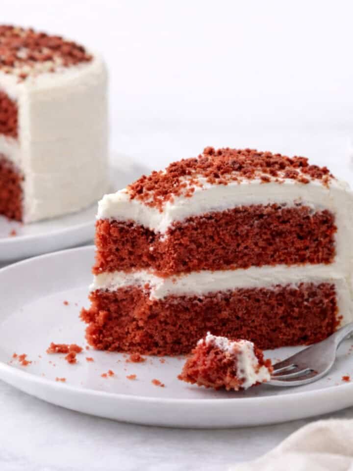 Vegan red velvet cake with cream cheese frosting on a white plate with a fork.