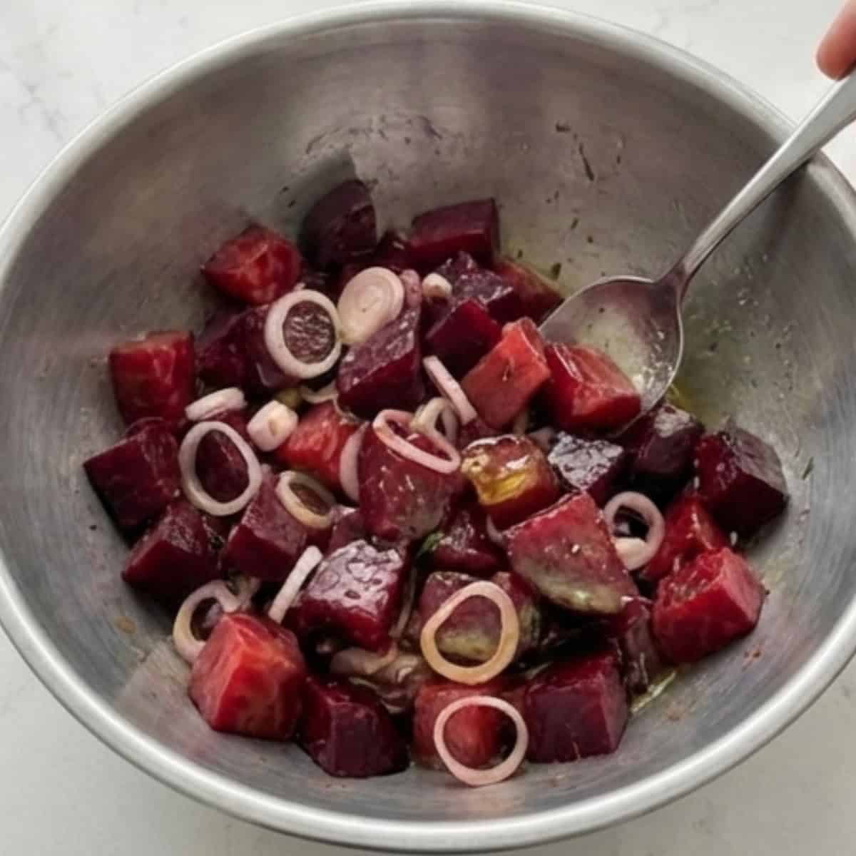 beets and shallots in a bowl being tossed with dressing