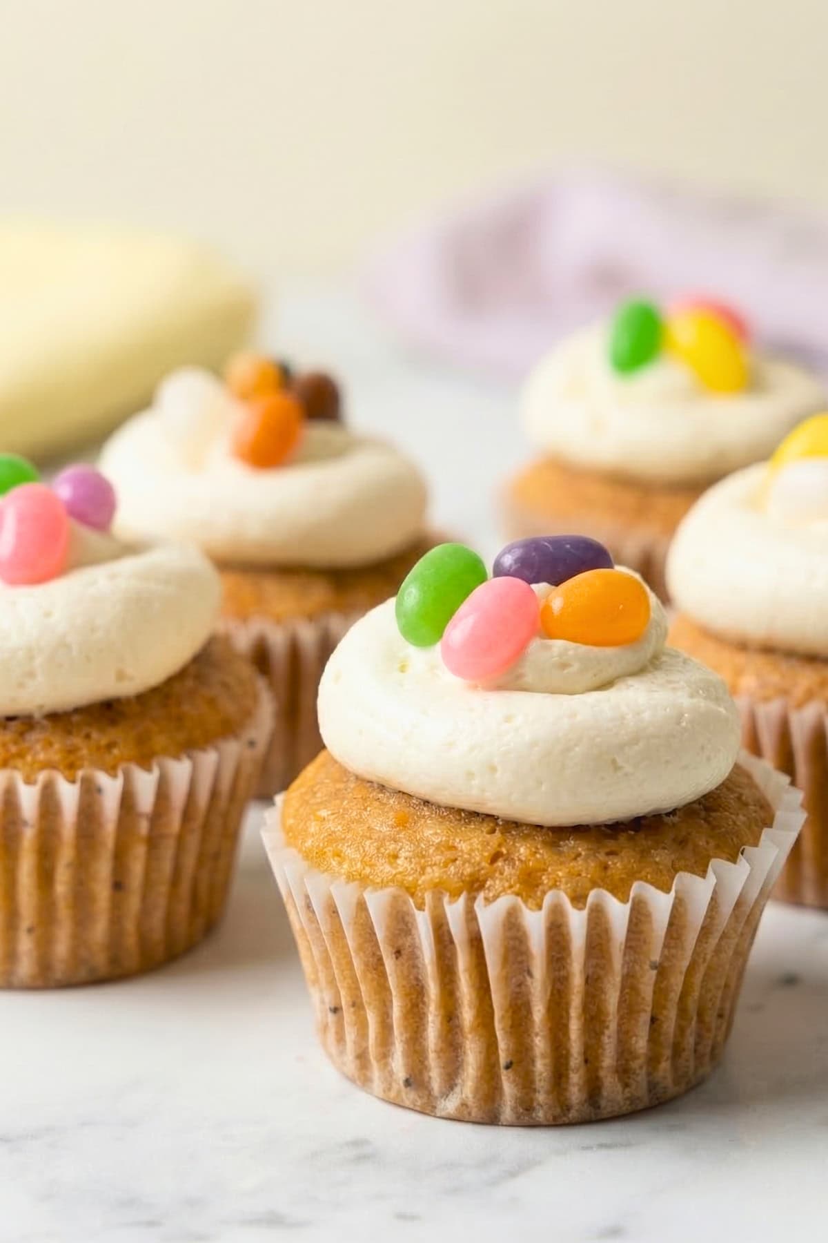 Five vegan vanilla Easter cupcakes topped with white vanilla buttercream frosting and colorful jelly beans.