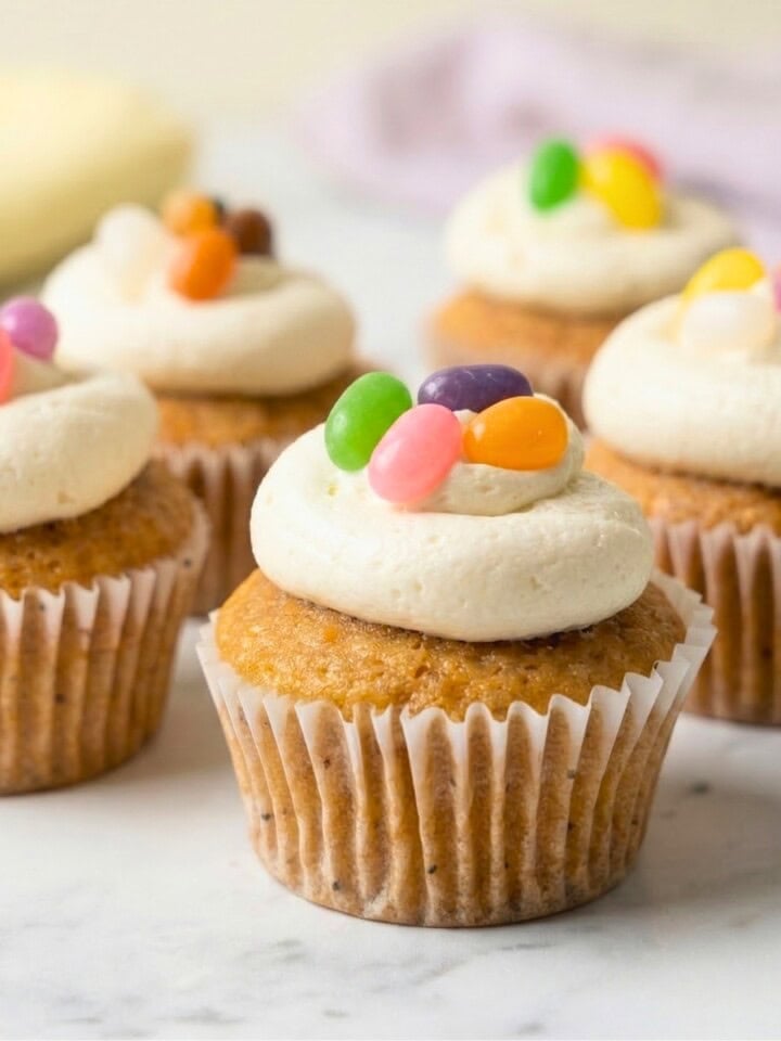 A five vegan vanilla Easter cupcakes topped with white vanilla buttercream frosting and colorful jelly beans.