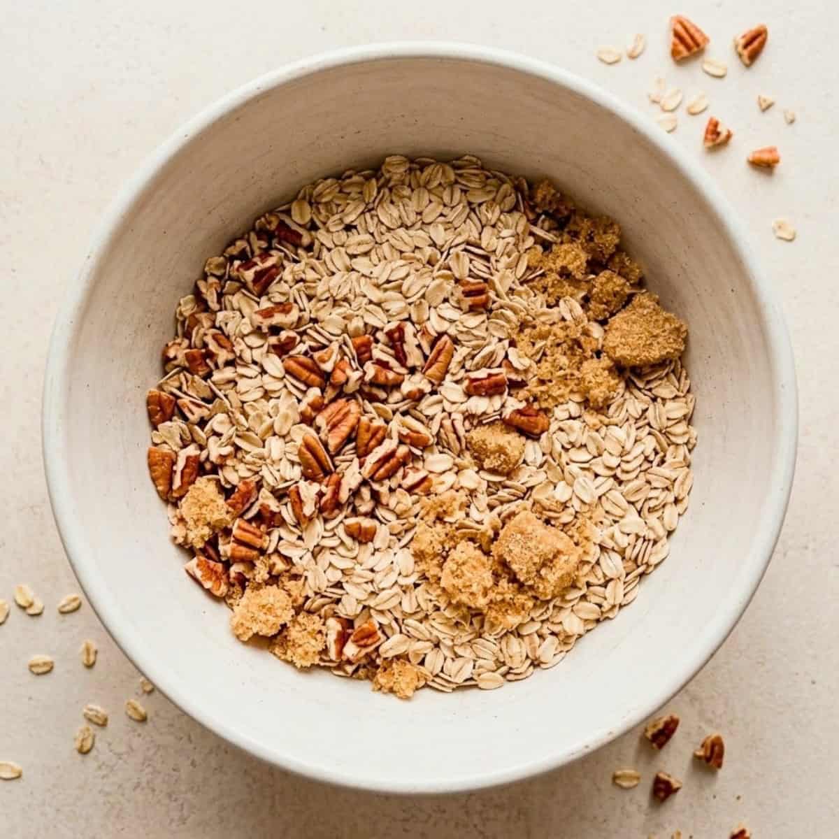Rolled oats, chopped pecans, and light brown sugar combined in a white mixing bowl.