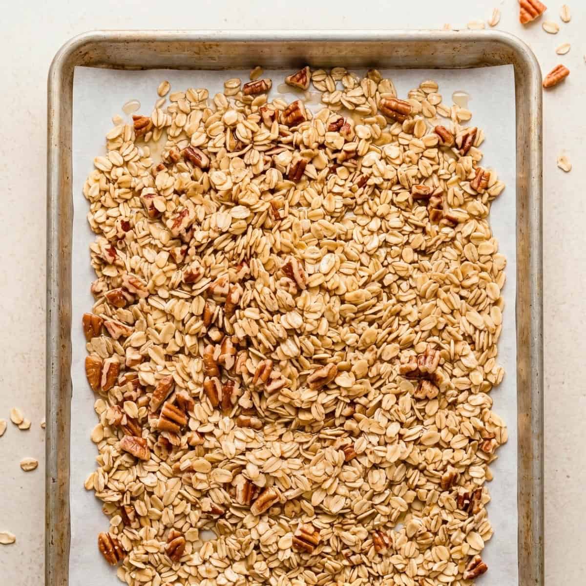 Unbaked maple pecan granola spread evenly on a parchment-lined baking sheet.