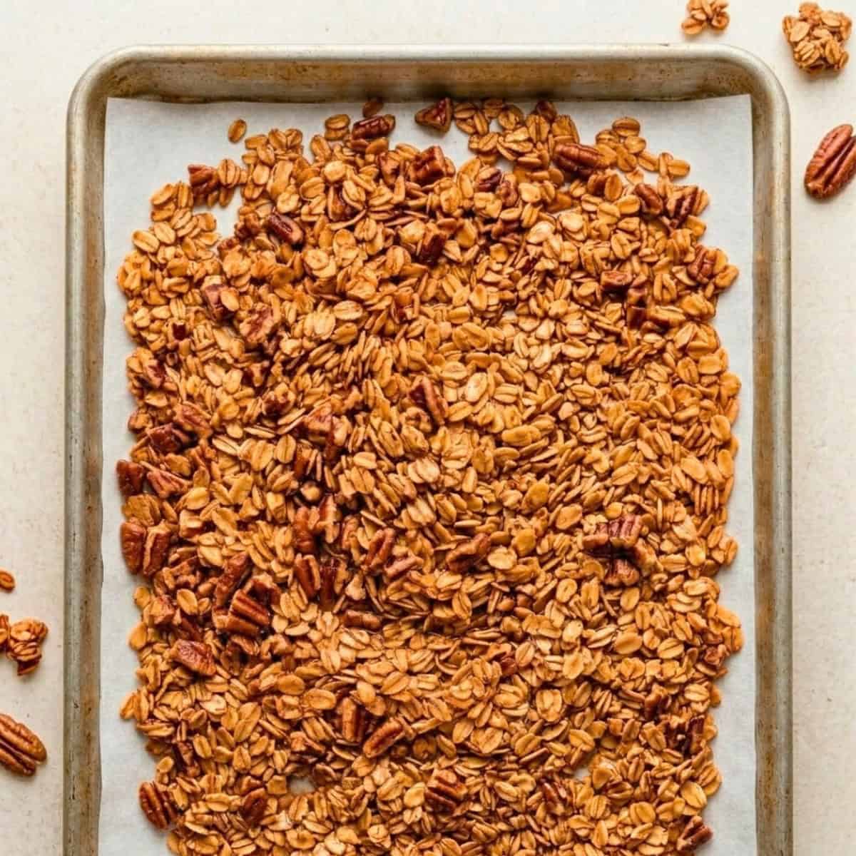 Golden brown maple pecan granola cooling on a parchment-lined baking sheet after baking.
