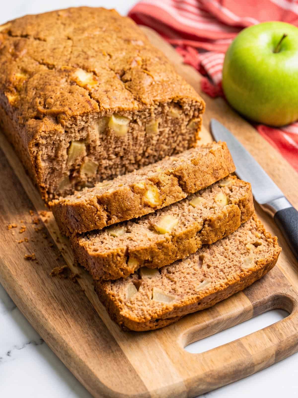Vegan apple bread loaf with several thick slices showing the soft texture and pieces of baked apple.