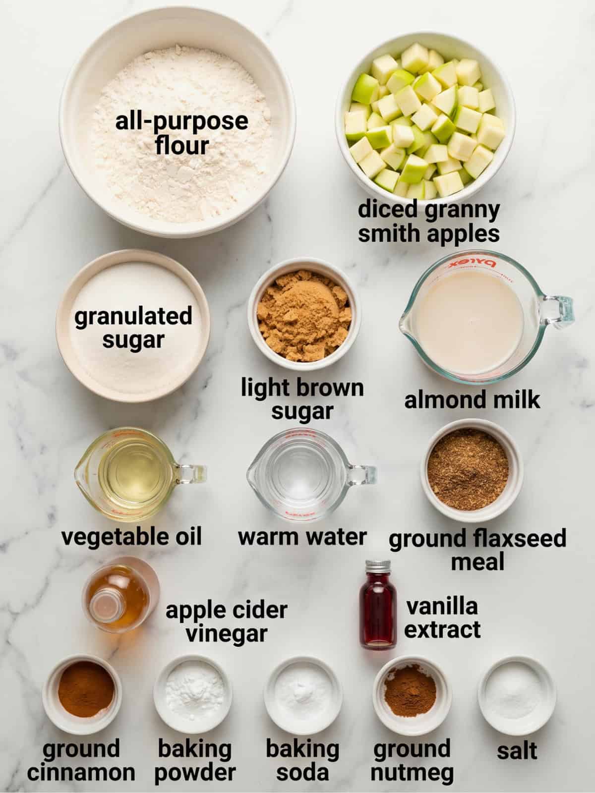 Overhead view of ingredients for vegan apple bread, including flour, diced apples, sugar, cinnamon, almond milk, oil, and ground flaxseed.