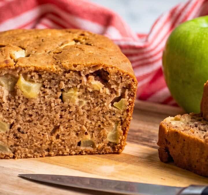 Vegan apple bread loaf with several thick slices showing the soft texture and pieces of baked apple.