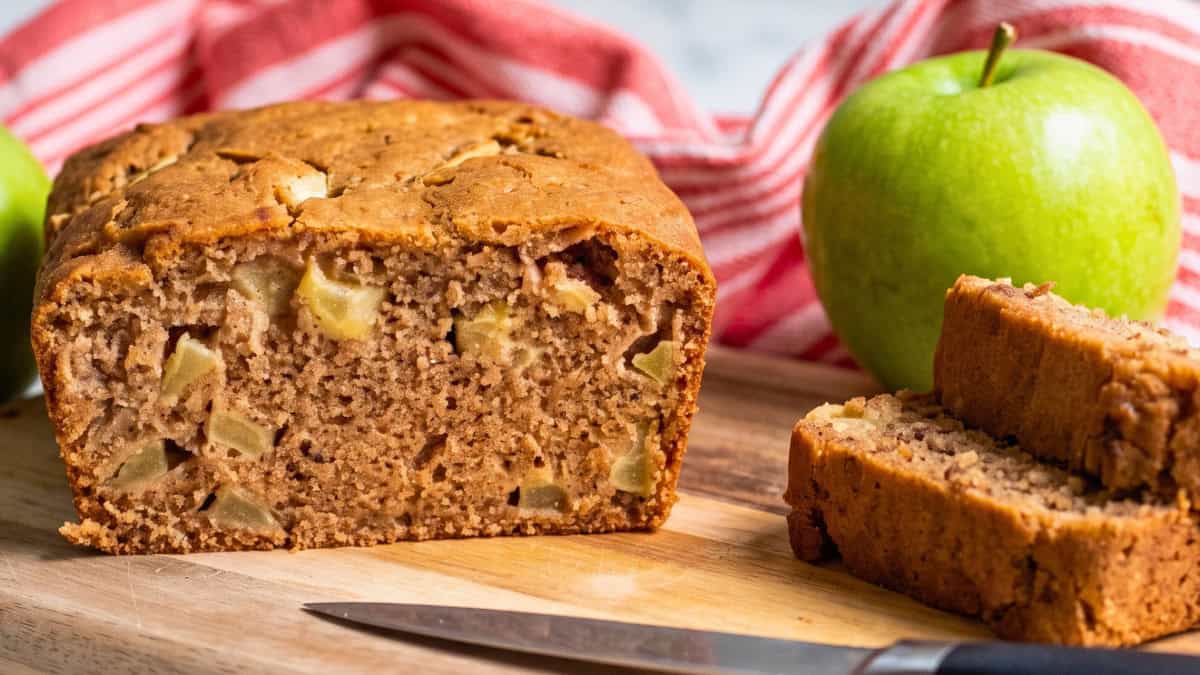 Vegan apple bread loaf with several thick slices showing the soft texture and pieces of baked apple.