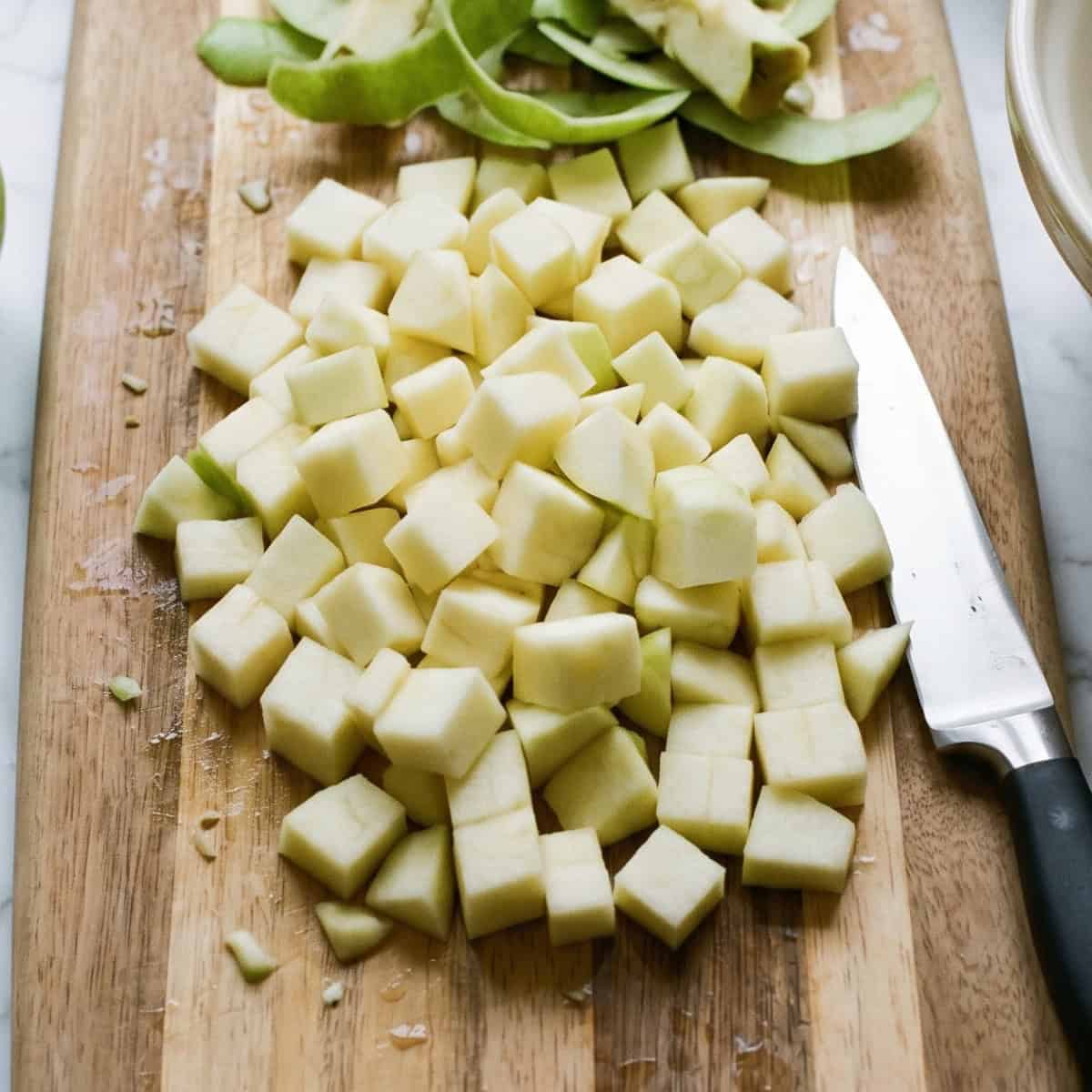 Peeled and diced Granny Smith apples on a wooden cutting board.