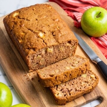 Homemade vegan apple cinnamon bread sliced on a wooden cutting board with fresh green apples.