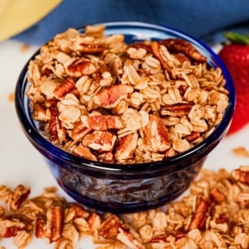Homemade maple pecan granola with toasted oats and crunchy pecans in a blue glass bowl.