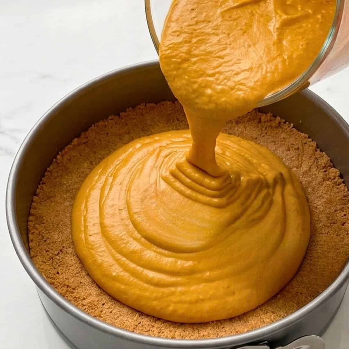Creamy pumpkin cashew cheesecake filling being poured into a graham cracker crust in a springform pan.