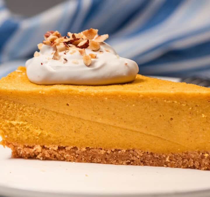 Slice of no-bake vegan pumpkin cheesecake with a graham cracker crust, whipped topping, and chopped pecans on a white plate.