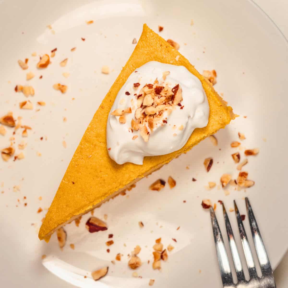 Overhead view of a slice of no-bake vegan pumpkin cheesecake topped with whipped cream and chopped pecans.