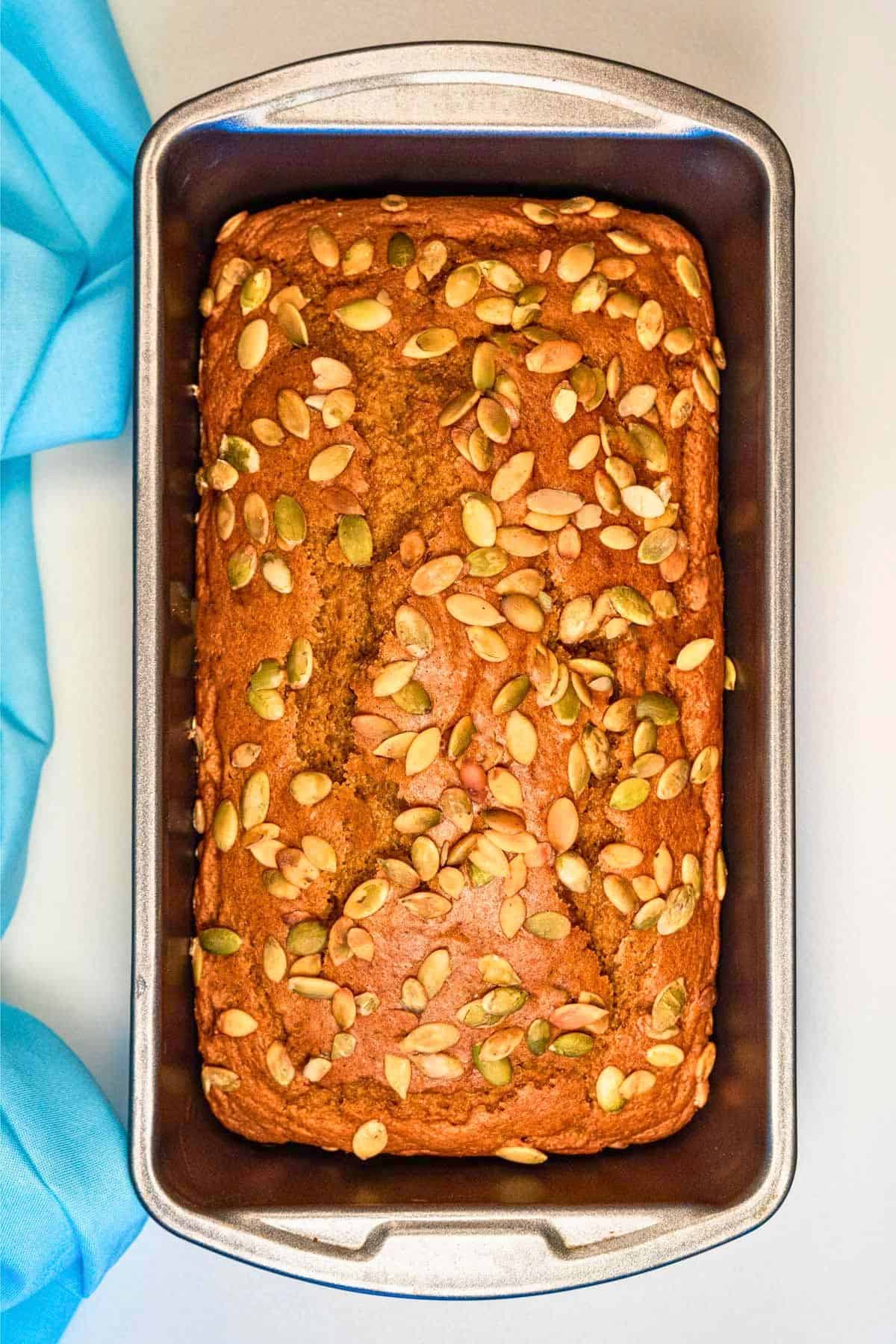 Baked vegan pumpkin loaf topped with pumpkin seeds in a loaf pan.