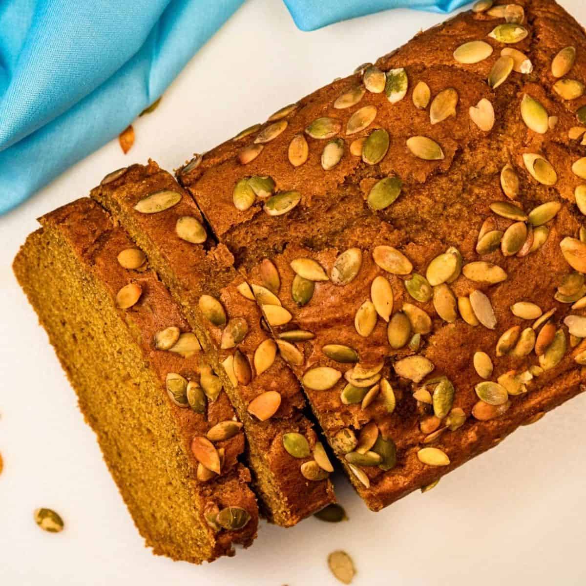 Sliced vegan pumpkin loaf topped with roasted pumpkin seeds.