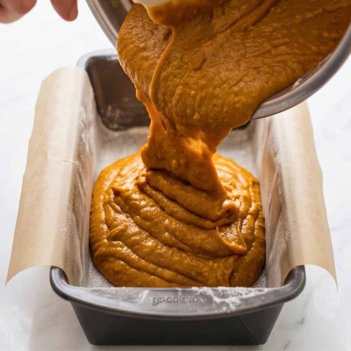 Pumpkin loaf batter being poured into a parchment-lined loaf pan.