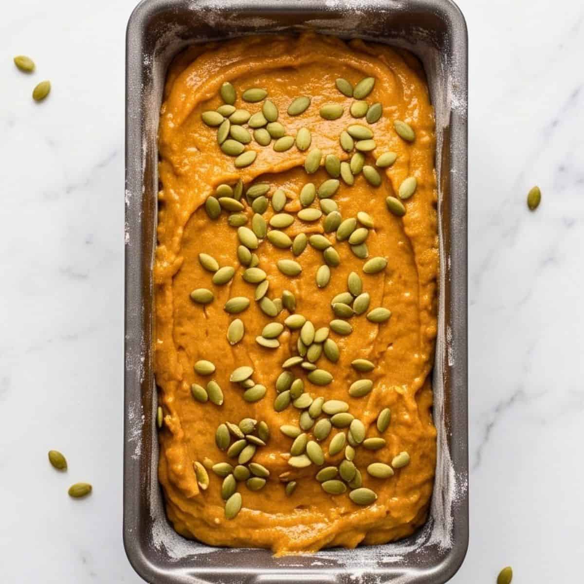 Pumpkin loaf batter topped with raw pumpkin seeds in a loaf pan.